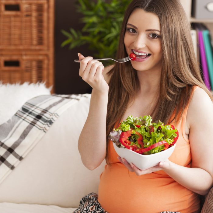 Pregnant smiling woman eating salad